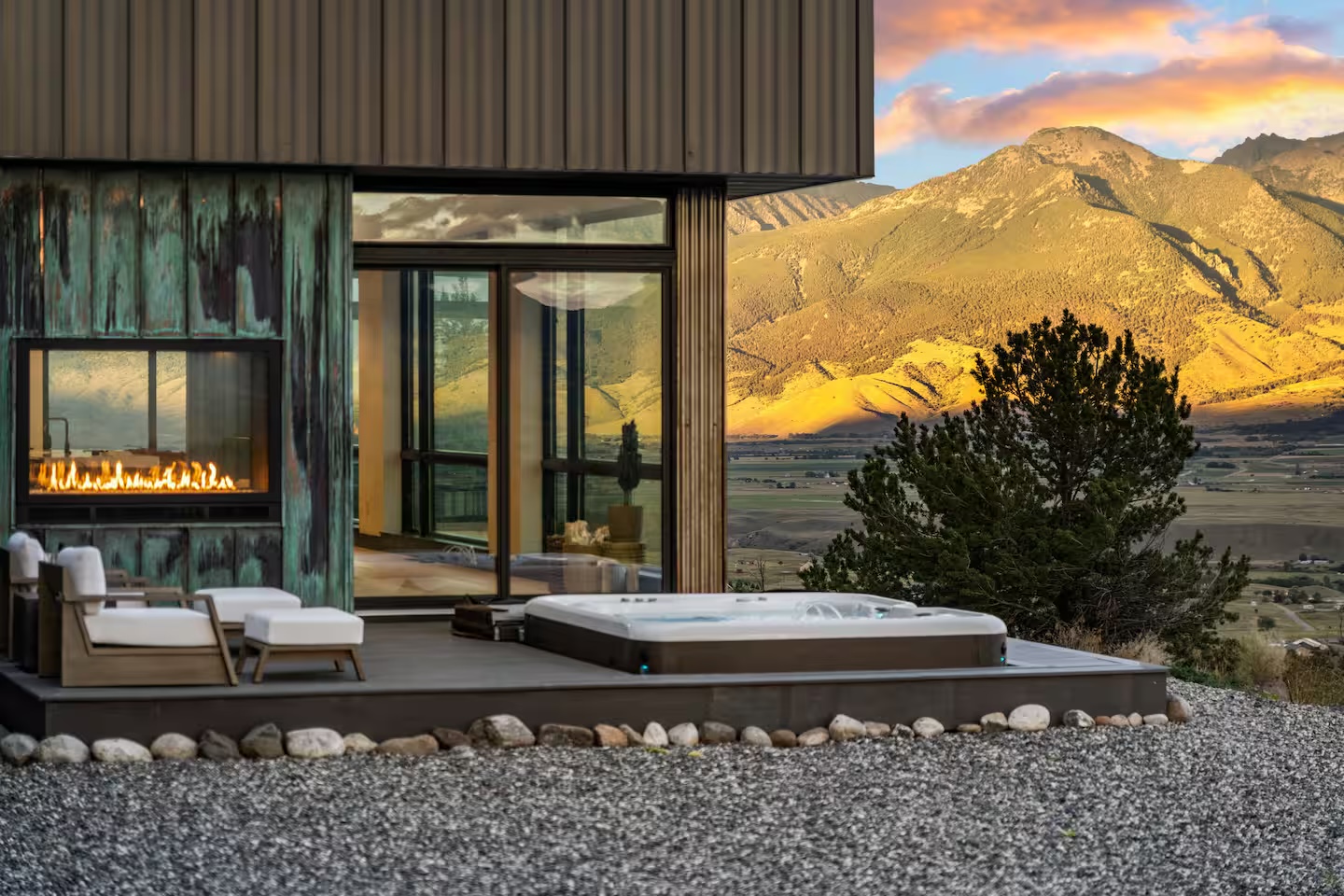 A modern Montana home with a fireplace and hot tub overlooking sunlit mountains
